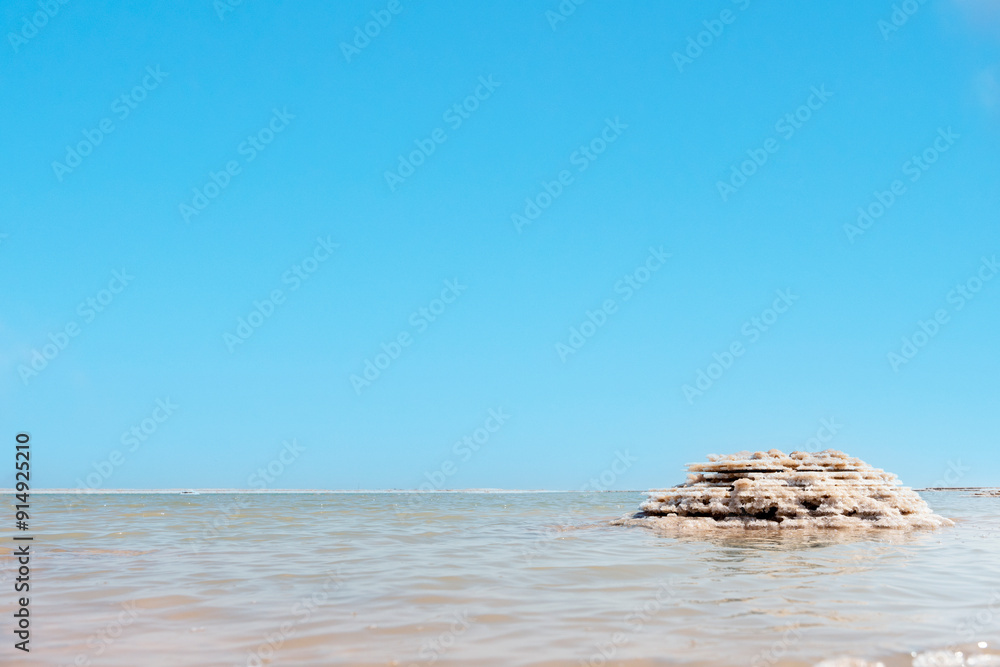 Calm waters and unique salt formations by Dead Sea under clear blue sky at a tranquil seaside location during midday Calm waters and unique salt formations by Dead Sea under clear blue sky at a tranquil seaside location during midday