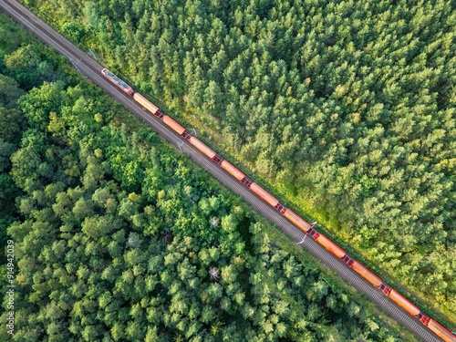 Aerial view of a red train transporting materials on tracks through a coniferous forest in Europe, delivery and transportation of goods, economic development, import, export, and railway transport.