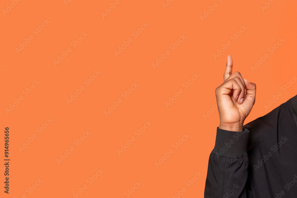 Person Raising Finger Against Vibrant Orange Background During Casual Moment Person Raising Finger Against Vibrant Orange Background During Casual Moment