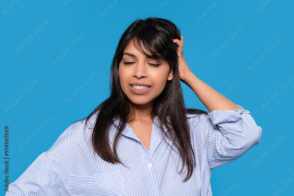 Young Woman in Striped Shirt Expressing Frustration Against Blue Background Young Woman in Striped Shirt Expressing Frustration Against Blue Background
