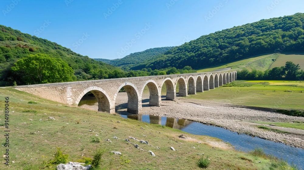 A long aqueduct stretches across a green field with mountains in the background. A long aqueduct stretches across a green field with mountains in the background.