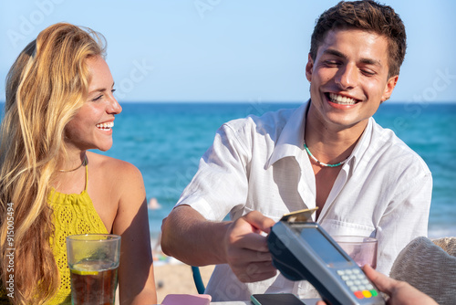 Smiling friends customer paying with contactless credit card in a restaurant. 
