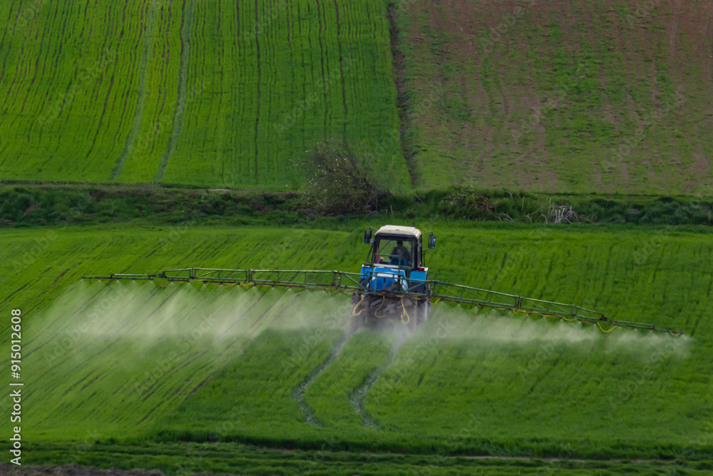 Fototapeta premium Aerial view of tractor spraying crop in green farm fields with pesticide