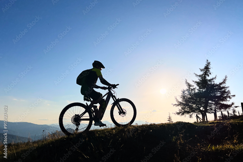 Cyclist man riding electric mountain bike outdoors. Male tourist biking along grassy trail in the mountains, wearing helmet and backpack. Concept of sport, active leisure and nature.