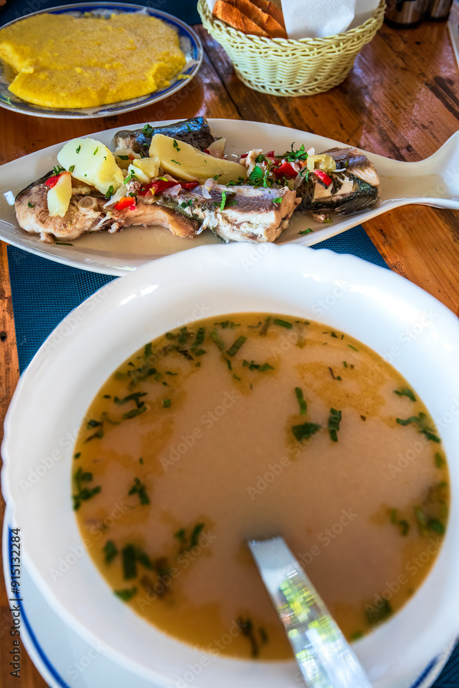 Bors de Peste, or Romanian Fish Soup, is a traditional dish served hot, garnished by a slice of crusty polenta (mamaliga).
