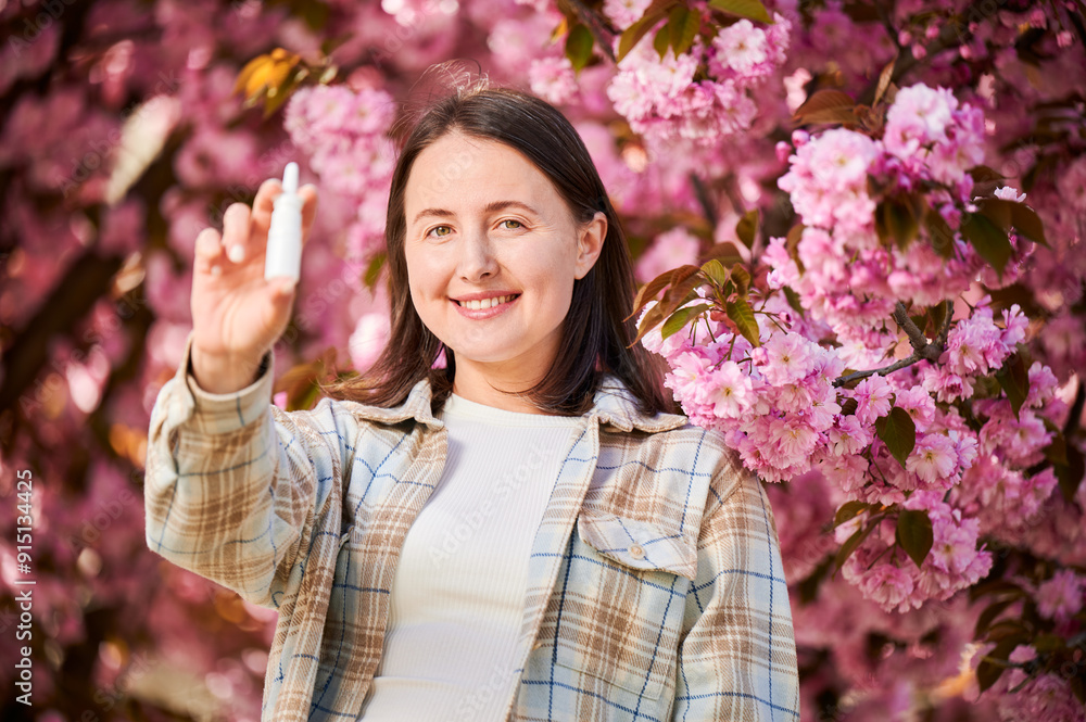 Woman allergic using medical nasal drops, suffering from seasonal allergy in blossoming garden. Smiling woman holding nasal spray near blooming tree. Spring allergy concept. Woman allergic using medical nasal drops, suffering from seasonal allergy in blossoming garden. Smiling woman holding nasal spray near blooming tree. Spring allergy concept.