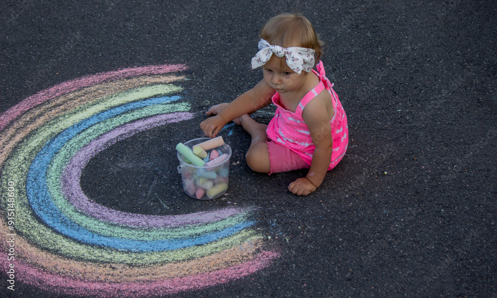 Naklejka premium a little girl draws a rainbow on the asphalt with chalk. Selective focus