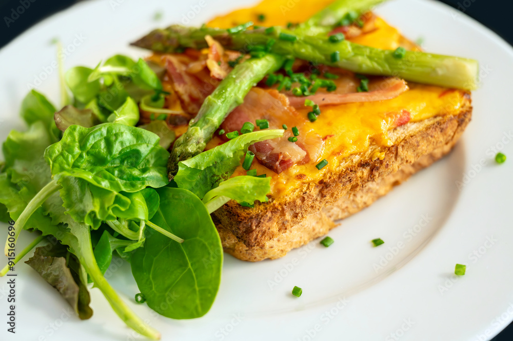 Fried toast with bacon and cheese, asparagus and fresh salad leaf on white plate, closeup.
