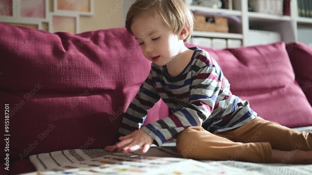 Cute toddler boy reading books on the sofa at home on a bright sunny afternoon Cute toddler boy reading books on the sofa at home on a bright sunny afternoon