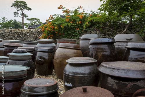 Summer view of crocks and trumpet creeper with orange flowers on the stonewall of tile-roofed house at Oeam Folk Village near Asan-si, South Korea 