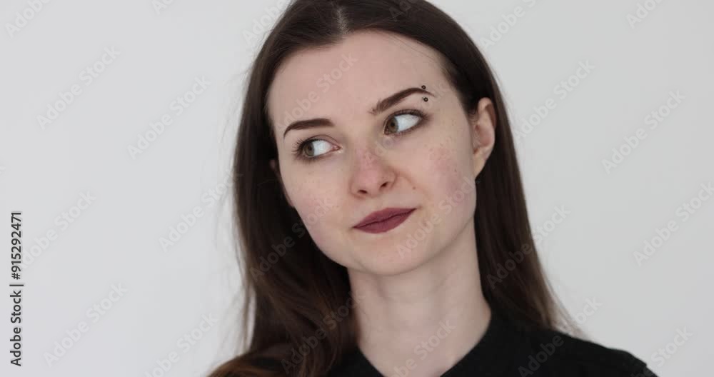 Female playfully looks hinting about need to leave party. Woman with eyebrow piercing uses body language to convey message against white Female playfully looks hinting about need to leave party. Woman with eyebrow piercing uses body language to convey message against white