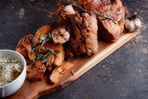 A set dish: a large fried piece of meat on the bone, country-style grilled potatoes, a mini salad of cabbage, bean sprouts, chia seeds and green onions. Original serving on a wooden cutting board. photo