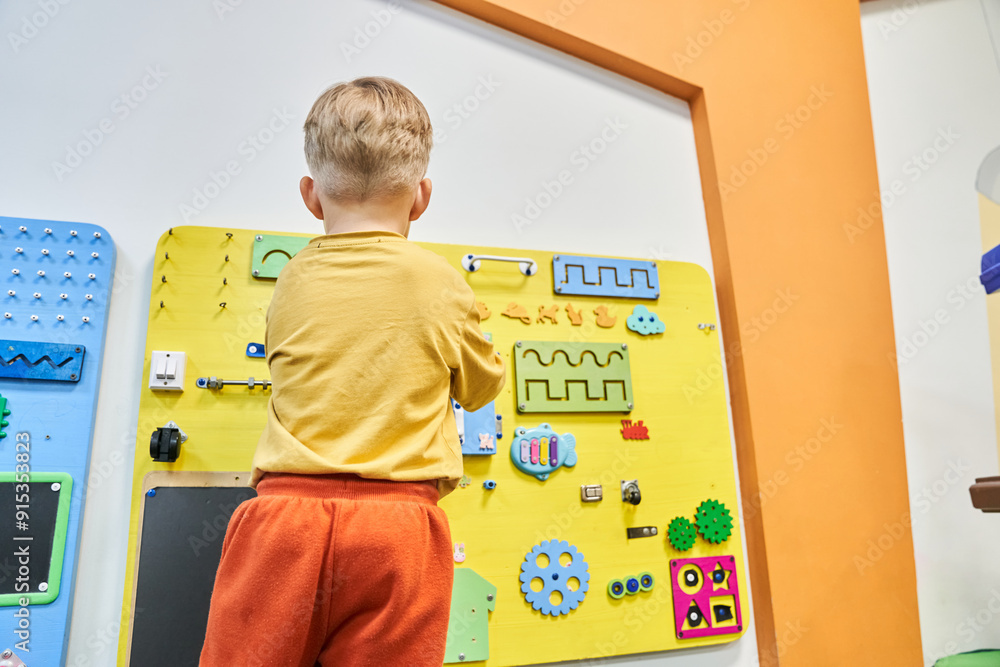 A child is playing a wooden maze on the wall. Educational logic toys for kids. An unrecognizable child with his back to the camera with a copy space. High quality photo A child is playing a wooden maze on the wall. Educational logic toys for kids. An unrecognizable child with his back to the camera with a copy space. High quality photo