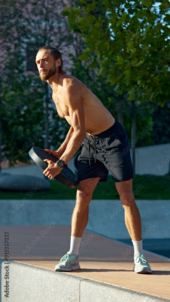 Obraz premium Early morning workout. Shirtless muscular man training in public park, doing exercises with heavy weights. Discipline and motivation. Concept of sport, active and healthy lifestyle, fitness