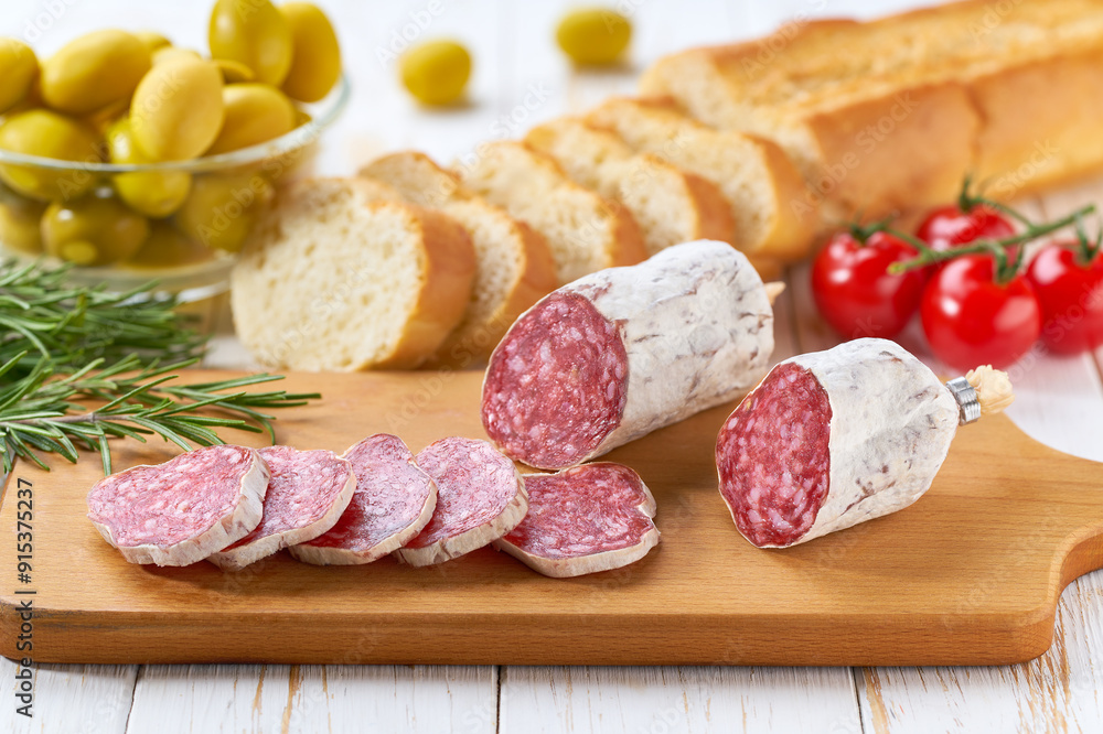 Traditional Spanish fuet spicy pork dry cured salami sausage with rosemary and baguet on a wooden table. Traditional Spanish fuet spicy pork dry cured salami sausage with rosemary and baguet on a wooden table.