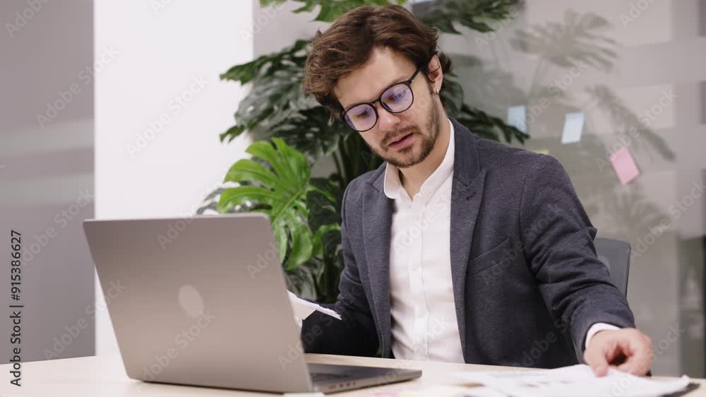 Ideal for demonstrating financial and trading activities. A young trader with a beard is focused on his laptop in a modern office. Ideal for demonstrating financial and trading activities. A young trader with a beard is focused on his laptop in a modern office.