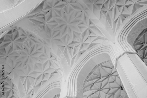 A black and white photograph capturing the complex geometry and elegance of a modern vaulted ceiling with distinctive arches.
