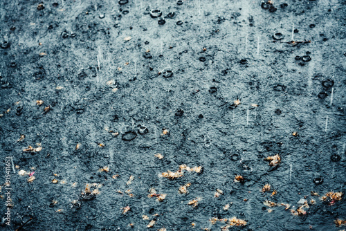 Heavy rain creates ripples and puddles on a dark asphalt street, with scattered small debris visible..Europe, Norway, Oslo, 09.05.2024