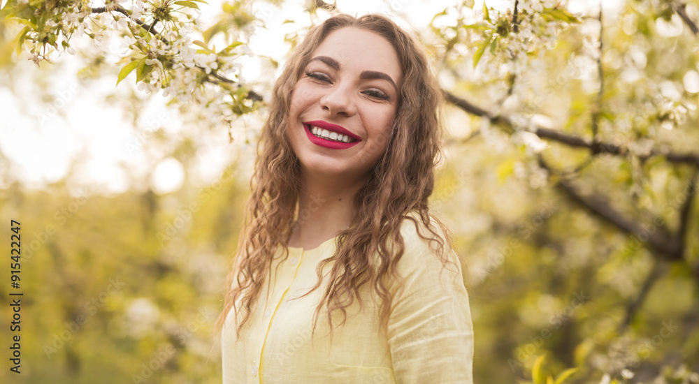 A cheerful woman in a yellow dress smiling joyfully in a blossoming orchard during a sunny day, portraying happiness and spring vibes. A cheerful woman in a yellow dress smiling joyfully in a blossoming orchard during a sunny day, portraying happiness and spring vibes.