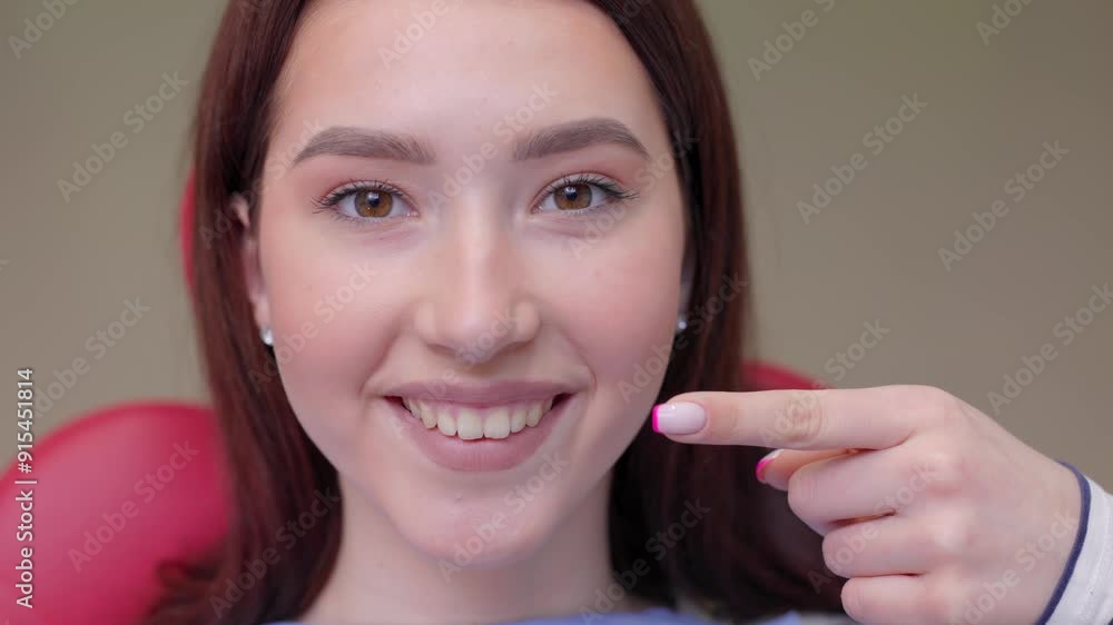 Cropped close up photo of young smiling girl, covered by napkin, pointing index finger on healthy toothy smile sitting at dental office chair. Healthcare teeth treatment Cropped close up photo of young smiling girl, covered by napkin, pointing index finger on healthy toothy smile sitting at dental office chair. Healthcare teeth treatment