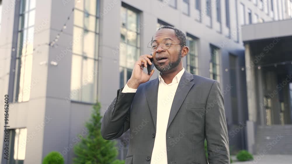 African American male in business suit talking on phone outside modern office building. Black man in glasses making a call while gesturing. Professional communication, businessperson, urban background African American male in business suit talking on phone outside modern office building. Black man in glasses making a call while gesturing. Professional communication, businessperson, urban background