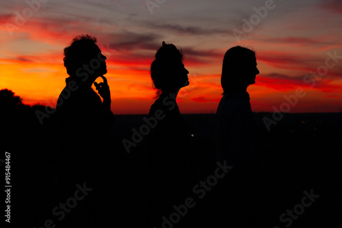 Red evening sky over people in darkness, some men and one woman, looking into the future