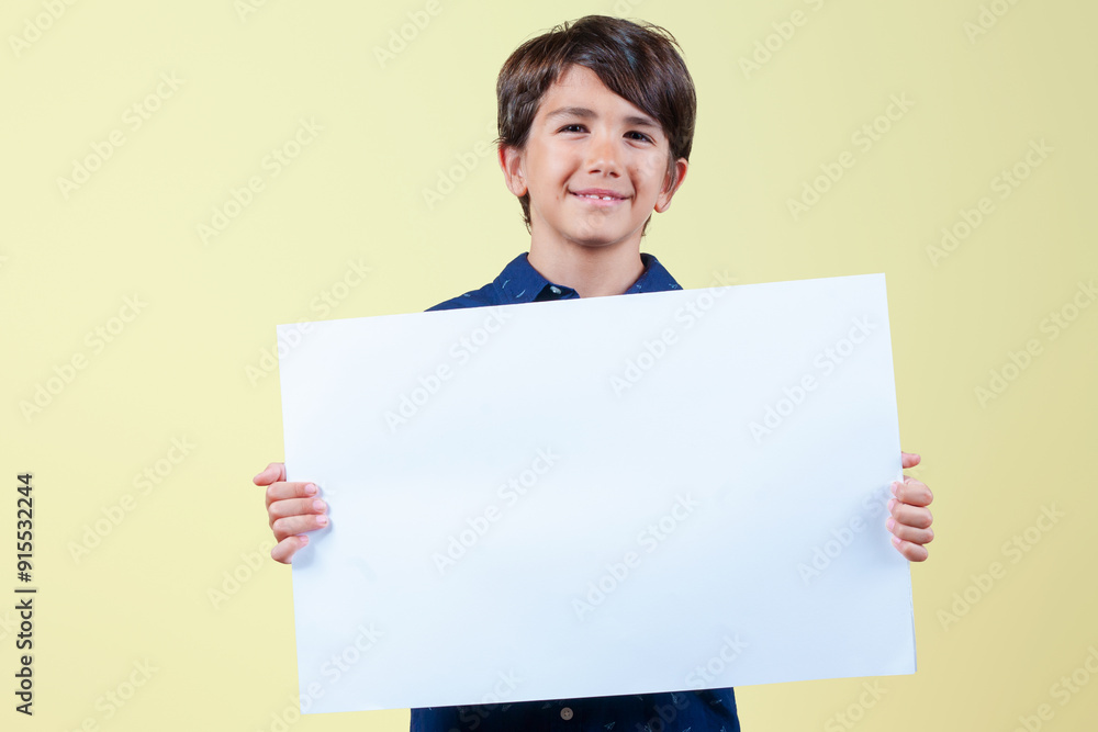 Cheerful kid showing white blank banner for business advertising and looking at camera isolated on yellow background. Cheerful kid showing white blank banner for business advertising and looking at camera isolated on yellow background.