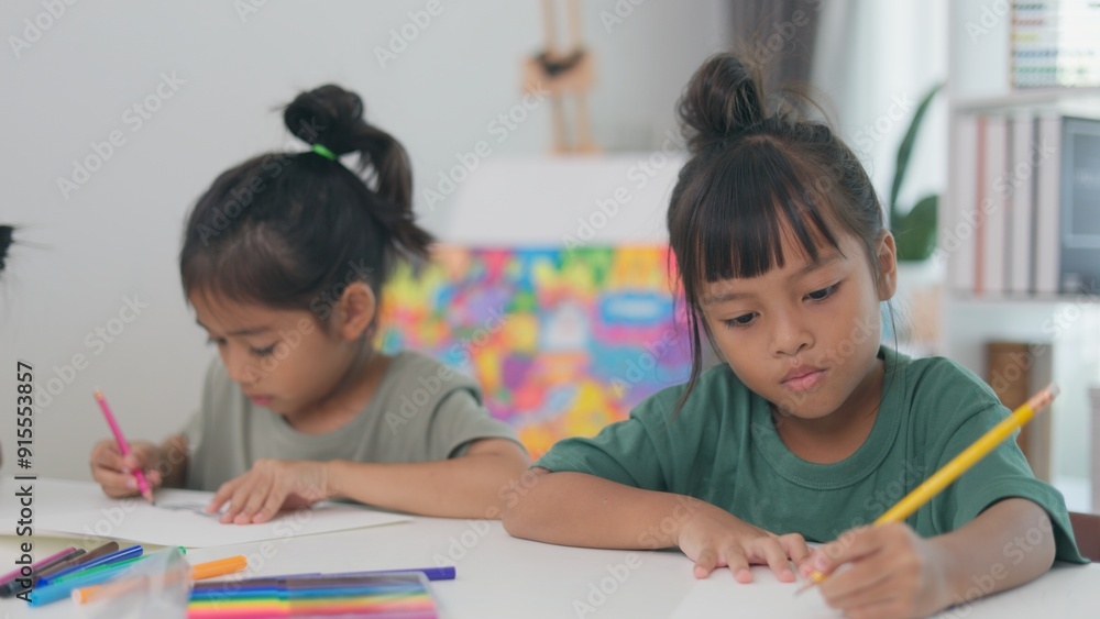 Two young girls are sitting at a table, drawing and writing Two young girls are sitting at a table, drawing and writing