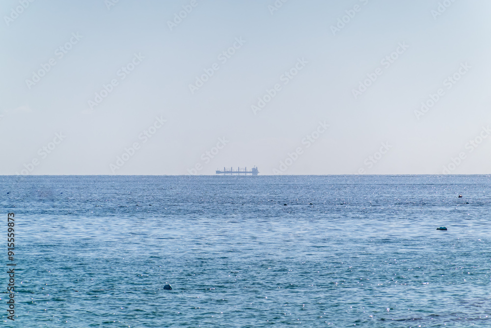 Calm blue sea with the silhouette of a large ship on the horizon Calm blue sea with the silhouette of a large ship on the horizon