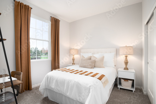 Fotografie A cozy bedroom with brown, orange, and white bedding, two lamps on white nightstands, and a small desk and chair
