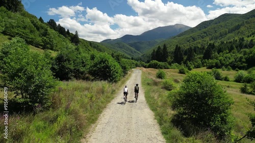 Drone view of cyclists are riding gravel bikes in scenic beauty of the mountains. Cycling on gravel roads or off-road. Active adventures and the concept of travel by bike. Gravel bike riding in nature