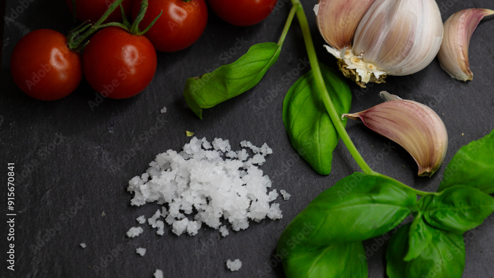 Juicy, aromatic, bright cherry tomatoes, sun-dried basil, spicy garlic with a slide of salt on a black stone plank. Copy space the text. Banner. Background Juicy, aromatic, bright cherry tomatoes, sun-dried basil, spicy garlic with a slide of salt on a black stone plank. Copy space the text. Banner. Background