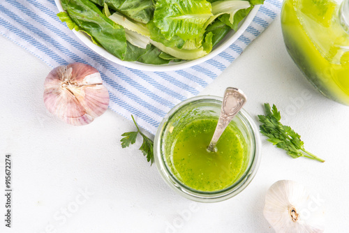 Culinary aromatic Green Herb Salad Dressing. Infused fresh Basil, parsley garlic olive oil for cooking dinner, with green salad on kitchen background copy space photo