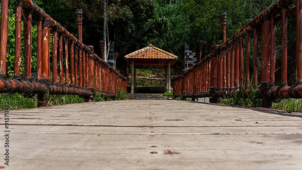 Low angle view of a wooden bridge leading to a bamboo gateway surrounded by lush green forest scenery. Low angle view of a wooden bridge leading to a bamboo gateway surrounded by lush green forest scenery.