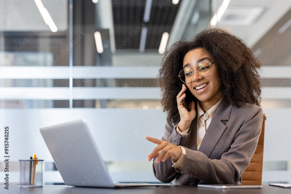 Young African American businesswoman on phone call while working on laptop in office Young African American businesswoman on phone call while working on laptop in office