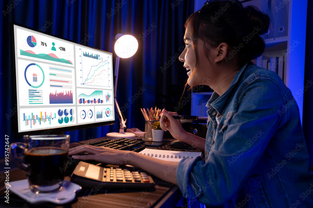 Smiling young beautiful asian creative looking on pc of profit of sales target report and writing on notebook for memo with planning invest new strategy market project at neon light night. Stratagem. Smiling young beautiful asian creative looking on pc of profit of sales target report and writing on notebook for memo with planning invest new strategy market project at neon light night. Stratagem.