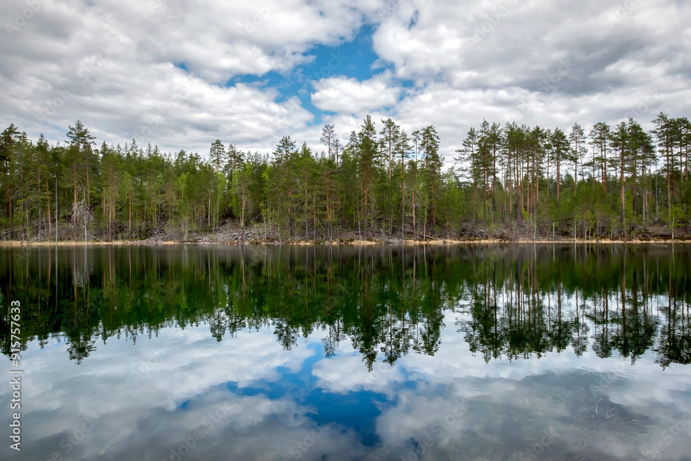 Quiet smooth beautiful lake in Karelia. Cloudy blue sky. Forest with trees and fir-trees. Quiet smooth beautiful lake in Karelia. Cloudy blue sky. Forest with trees and fir-trees.