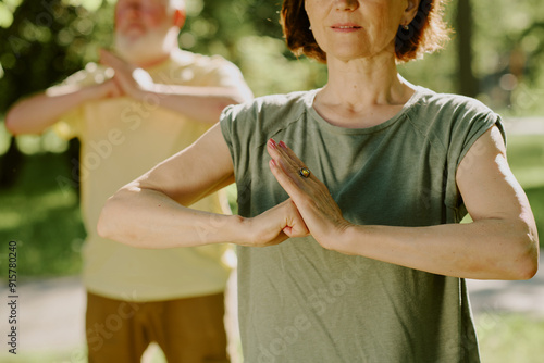 Medium close up of toned arms of senior woman in open hand vs closed fist position, senior man practicing same pose in blurred background