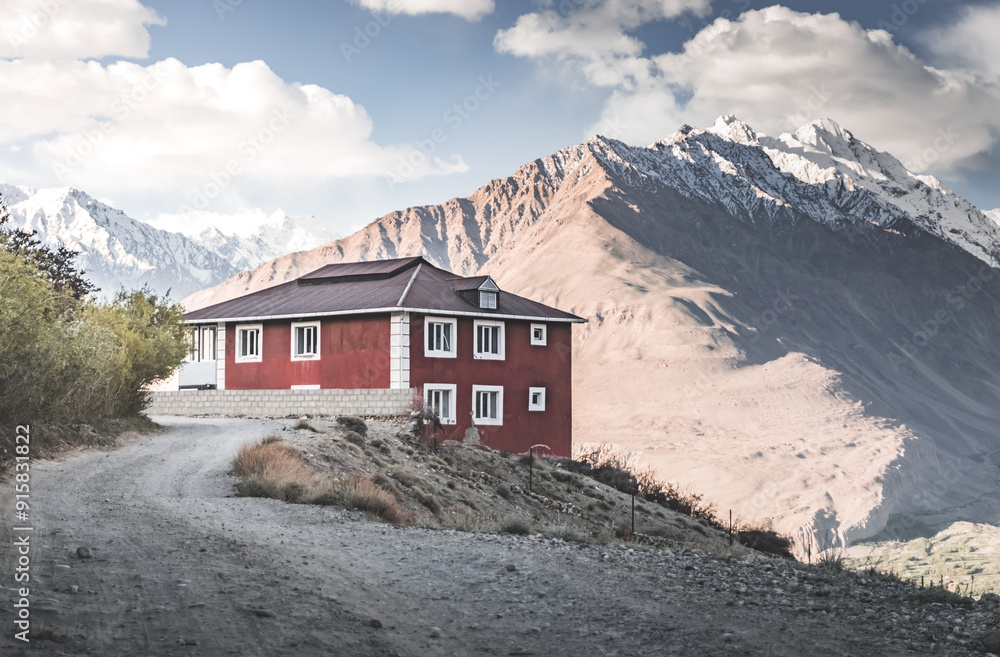 A red house stands on a mountain cliff against the background of a panorama of the rocky mountain range of the Tien Shan with snow and glaciers, landscape with building in the evening in Pamir A red house stands on a mountain cliff against the background of a panorama of the rocky mountain range of the Tien Shan with snow and glaciers, landscape with building in the evening in Pamir