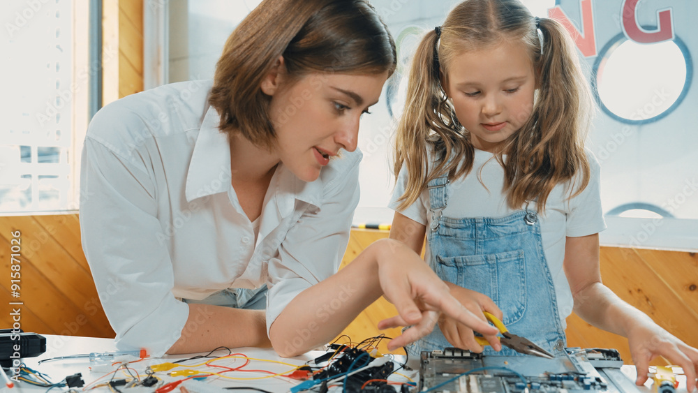 Fototapeta premium Young smart caucasian teacher teaching students about part of electronic board. Expert girl learn about digital electrical tool and fixing motherboard at table with chips and wires placed. Erudition.