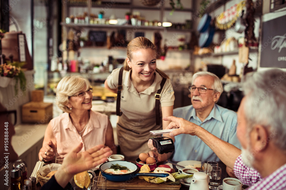 Senior man paying with smartphone for meal with friends at a restaurant Senior man paying with smartphone for meal with friends at a restaurant