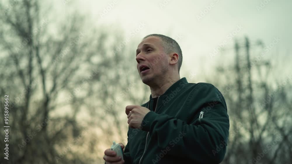 A close view of a man using a white inhaler, with background of trees, and sky in view