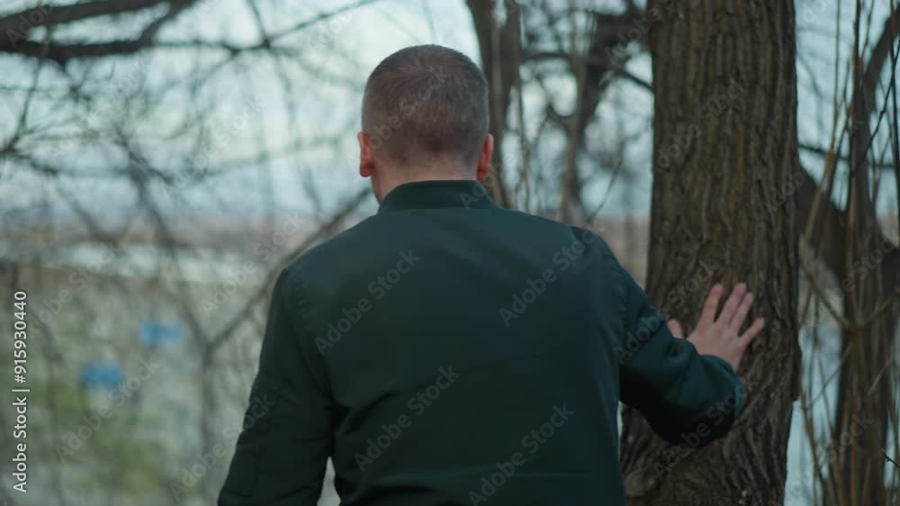 Blurred close-up of a man in a green jacket outdoors with a background of tangled branches and distant scenery, with someone walked by and touch the tree Blurred close-up of a man in a green jacket outdoors with a background of tangled branches and distant scenery, with someone walked by and touch the tree