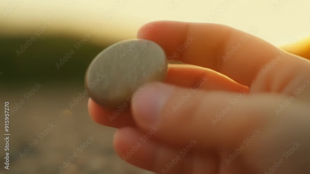 Low angle of a childs hand picking up a smooth pebble marveling at the polished surface and rounded shape. Low angle of a childs hand picking up a smooth pebble marveling at the polished surface and rounded shape.