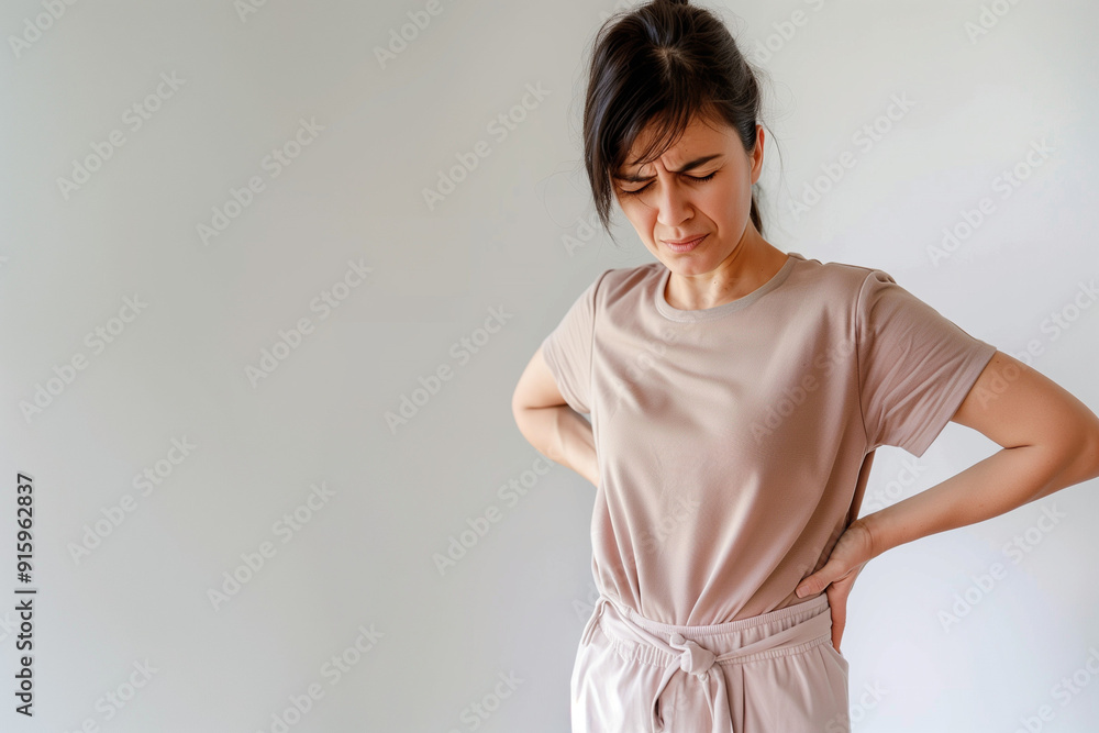 A woman with back pain, expressing discomfort while standing. A woman with back pain, expressing discomfort while standing.