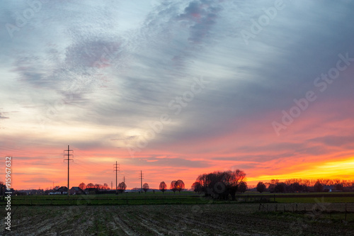 The setting sun in the flemish country side colors the sky intensely yellow and orange.