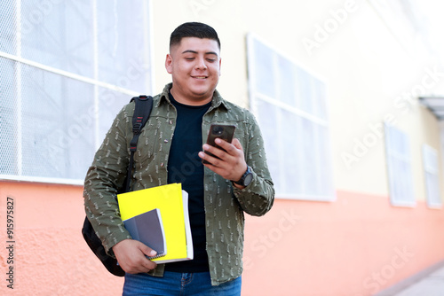 young latin american student holding books and smartphone outside the university