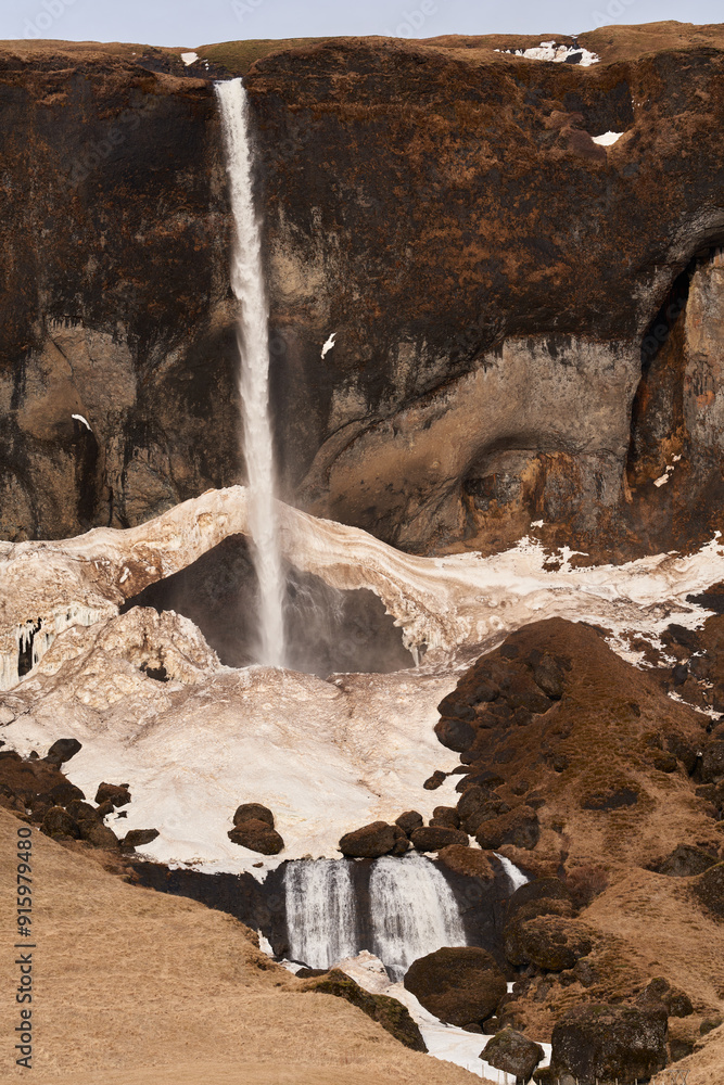 Obraz premium Water cascading down a rocky cliff in iceland with snow and ice on the ground