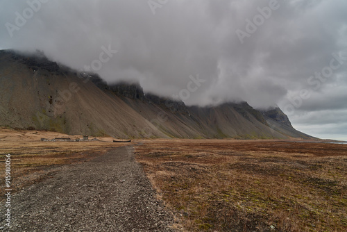 Gravel road leading to dramatic mountain range covered by clouds in iceland