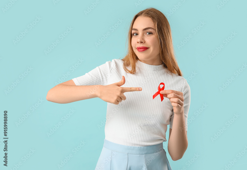 Young woman pointing at red ribbon on blue background. AIDS concept Young woman pointing at red ribbon on blue background. AIDS concept